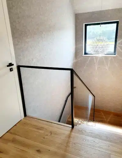 Minimalistyczna balustrada szklana ze stalowym pochwytem przy drewnianych schodach w Wejherowie.