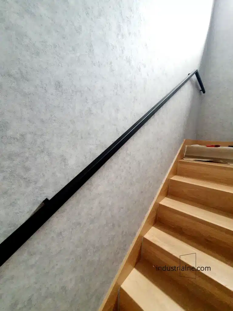Detal czarnej poręczy schodowej ze stali na tle betonowej ściany w Wejherowie.